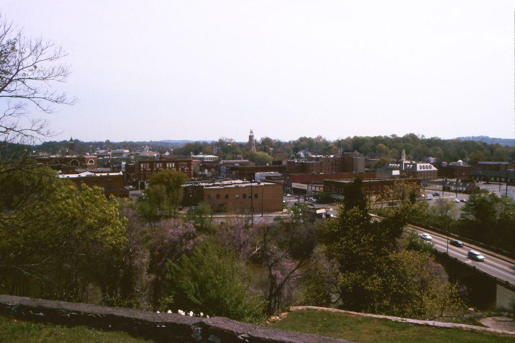 Eine Stadtansicht mit Gebäuden, Bäumen, Polen, Straßen, Fahrzeugen und einem Himmel.