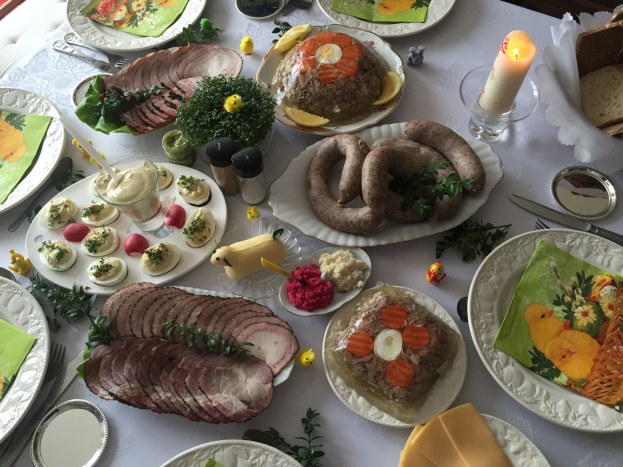 Ein langer Tisch mit einer Vielzahl von Gerichten, Besteck und Kerzen, umgeben von Stühlen, die auf ein traditionelles deutsches Osteressen hinweisen.