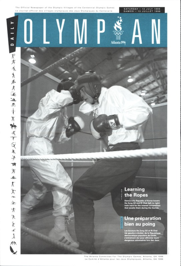 Zwei Boxer im Ring, mit Helmen und Handschuhen, Seilen und Lichtern und "Olympian Magazine" Text oben und unten.
