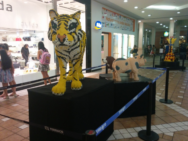 Statuen von Tieren auf schwarzen Kisten umgeben von Pfählen mit Gummibändern, mit Geschäften, die Taschen, Schuhe und andere Gegenstände anbieten, und Menschen, die herumlaufen.