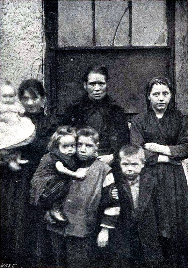Ein altes Schwarz-Weiß-Foto einer Familie, die vor einer Wand mit einem Fenster posiert, mit dem Text "Mother Teresa mit ihren Kindern" am unteren Rand.