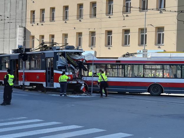Eine rote und weiße Straßenbahn nach einem Zusammenstoß auf der Straße mit ein paar Menschen in der Nähe und einem Gebäude im Hintergrund.
