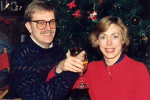 Ein Paar lächelt, whährend es Gläser Wein hält, mit einem Weihnachtsbaum im Hintergrund.