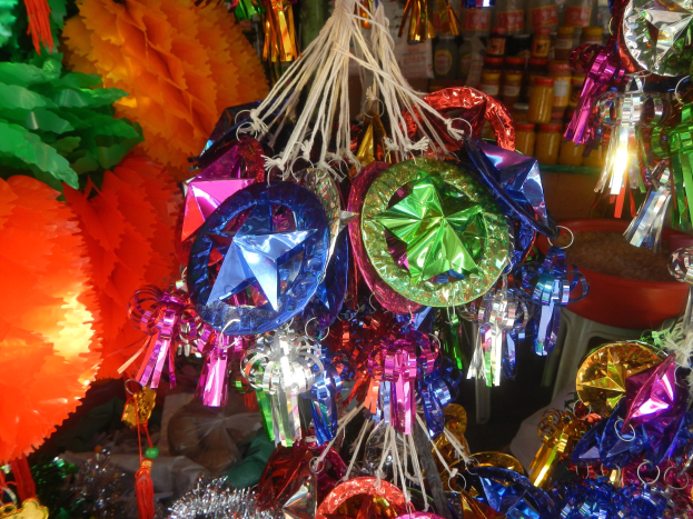 Farbenfrohe Festschmuckdekorationen, darunter Laternen und Bänder, hängen von der Decke über Regalen mit Flaschen im Hintergrund.