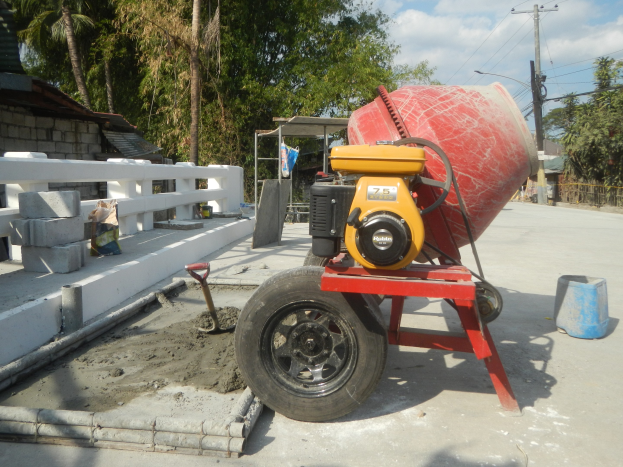 Betonmischer auf einem Zementlaster umgeben von Baustoffen und einer Wohngegend bei einem bewölkten Himmel.