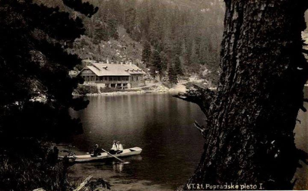 Ein Schwarz-Weiß-Foto von zwei Menschen in einem Kanu auf einem See in Popradskie, Polen, umgeben von Bäumen und einem Haus im Hintergrund, aufgenommen in den 1920er Jahren, wobei beide Personen Paddel halten.