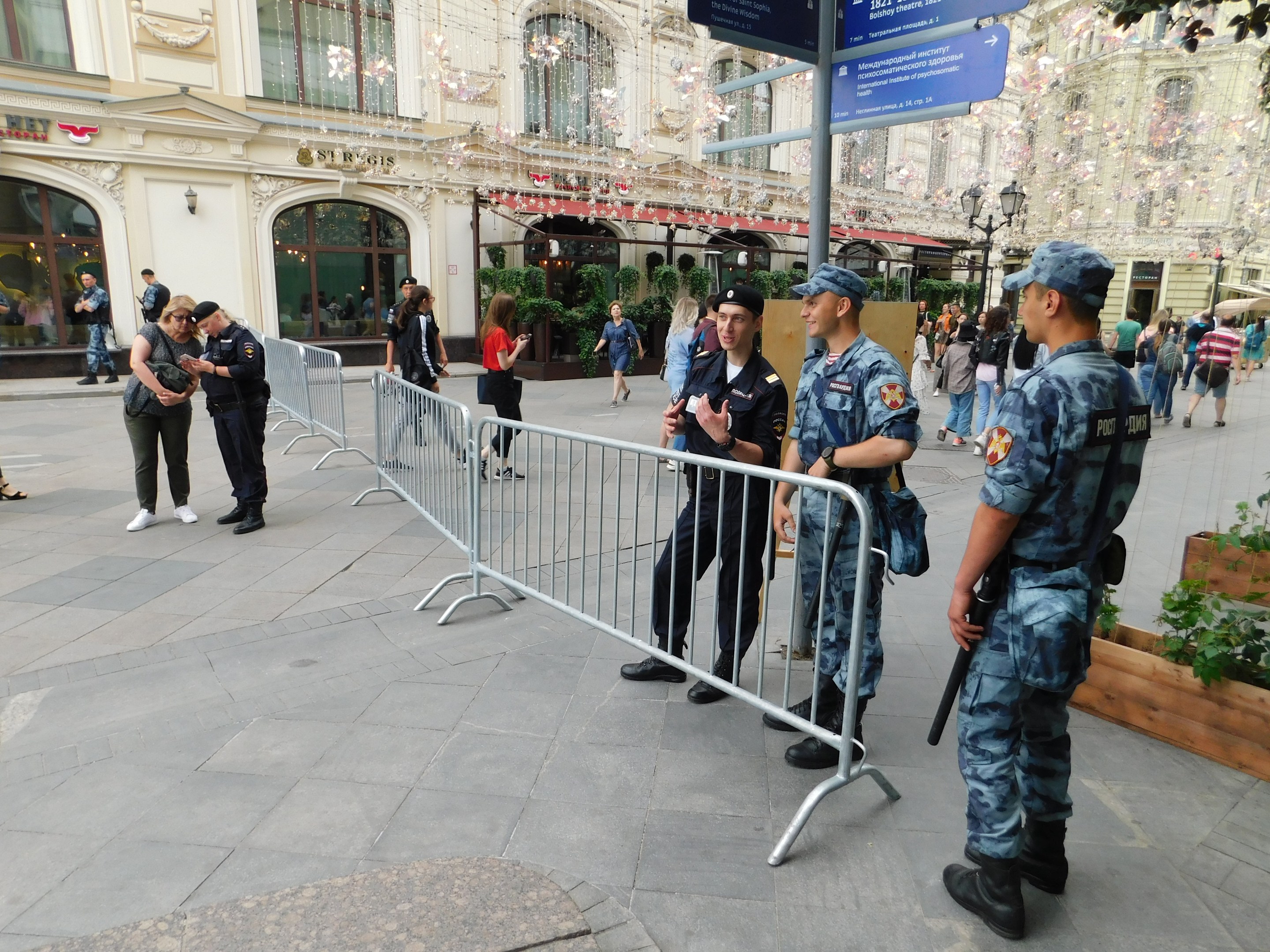 Polizisten in Uniform stehen hinter Absperrungen und blicken auf eine Menge, von der einige Kapuzen tragen und Waffen halten, während sie eine Anti-Terror-Operation in Wien, Österreich, durchführen.