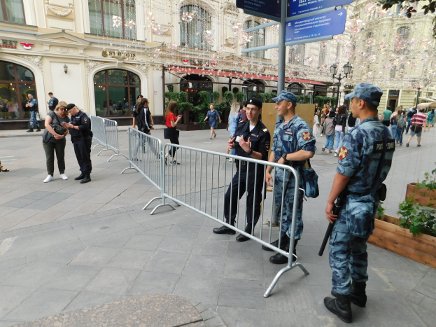 Polizisten in Uniform stehen hinter Absperrungen und blicken auf eine Menge, von der einige Kapuzen tragen und Waffen halten, während sie eine Anti-Terror-Operation in Wien, Österreich, durchführen.