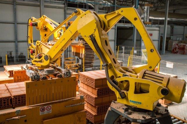 Großes Industriegebäude mit gestapelten Kisten, Kränen an der Decke, Zaun, Pfählen und einer fernen Wand in einer Fertigungsumgebung.