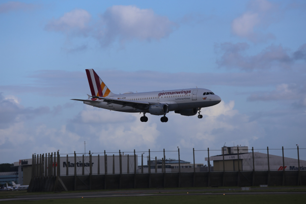 Germanwings Airbus A320-200 startet von Frankfurt Airport, mit Gras, einem Zaun, Gebäuden, Bäumen und einem bewölkten Himmel im Hintergrund.