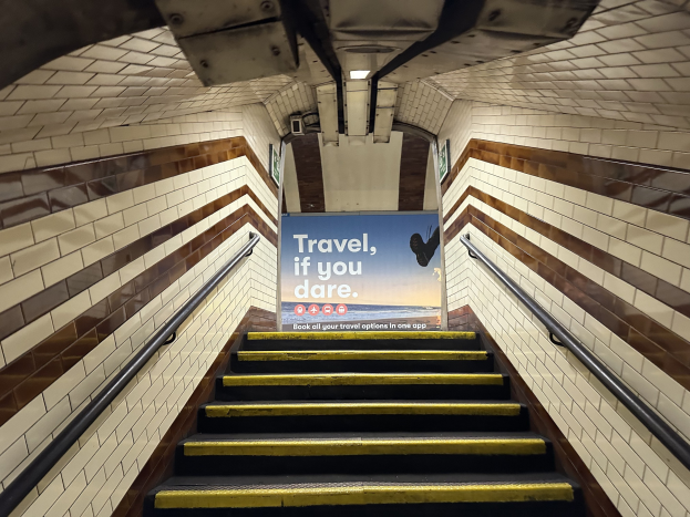 Eine Treppe in einer U-Bahn-Station mit einem Schild oben, das 'Reise, wenn du wagst' lautet, flankiert von Geländern und sichtbaren Stationswänden.