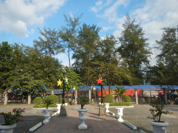 Ein Park mit Topfpflanzen und Bäumen, umgeben von Straßenlaternen, Straßenlaternen, Dekorationsgegenständen und Grills, mit einem bewölkten Himmel im Hintergrund.