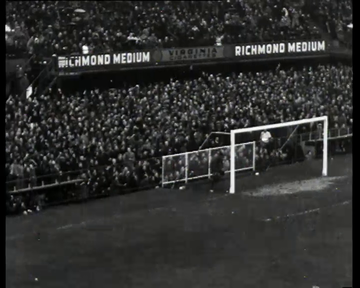 Ein Schwarz-Weiß-Foto eines Fussballspiels in einem Stadion mit Zuschauern auf den Rängen und Spielern auf dem Feld, das ein Tor mit Netz und eine Anzeigetafel mit der Aufschrift "West Ham United v West Ham United - FA Cup Final" zeigt.