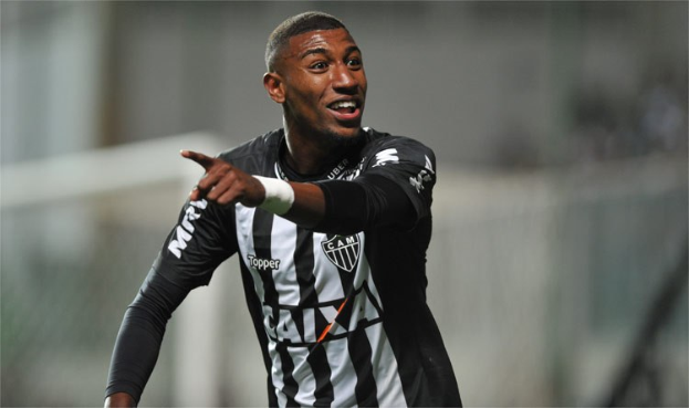 Ein Fußballspieler in einem schwarz-weißen gestreiften Trikot lächelt beim Feiern eines Tors, mit einem unscharfen Hintergrund.