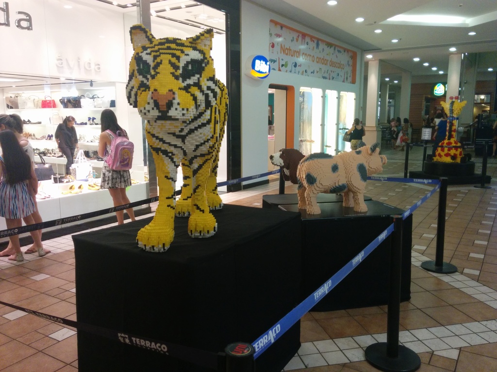 Tierstatuen auf schwarzen Kisten mit Stangen und Gummigürteln drumherum, umgeben von Geschäften mit Taschen, Schuhen und anderen Artikeln, mit Menschen und Deckenleuchten im Hintergrund.