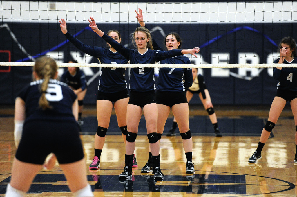 Drei Mädels bei einem Volleyballspiel auf dem Feld stehend, ein Netz vor ihnen und ein Zaun im Hintergrund.