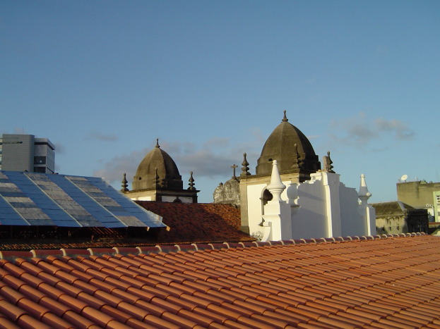 Eine Stadtansicht mit mehreren Gebäuden im Vordergrund, einem klaren blauen Himmel im Hintergrund und Solarpanels auf dem Dach eines Gebäudes.