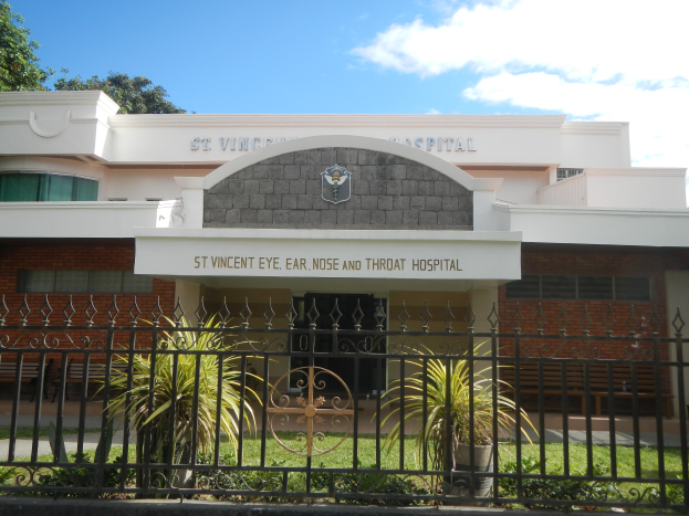 Ein Gebäude mit einer Tafel, auf der "St. Vincent Augen-, Ohren-, Nasen- und Hals-Nasen-Ohren-Krankenhaus" steht, mit Fenstern, einer Tür, einem Metallzaun, Topfpflanzen, Gras, einem Weg und Bäumen unter einem bewölkten Himmel.