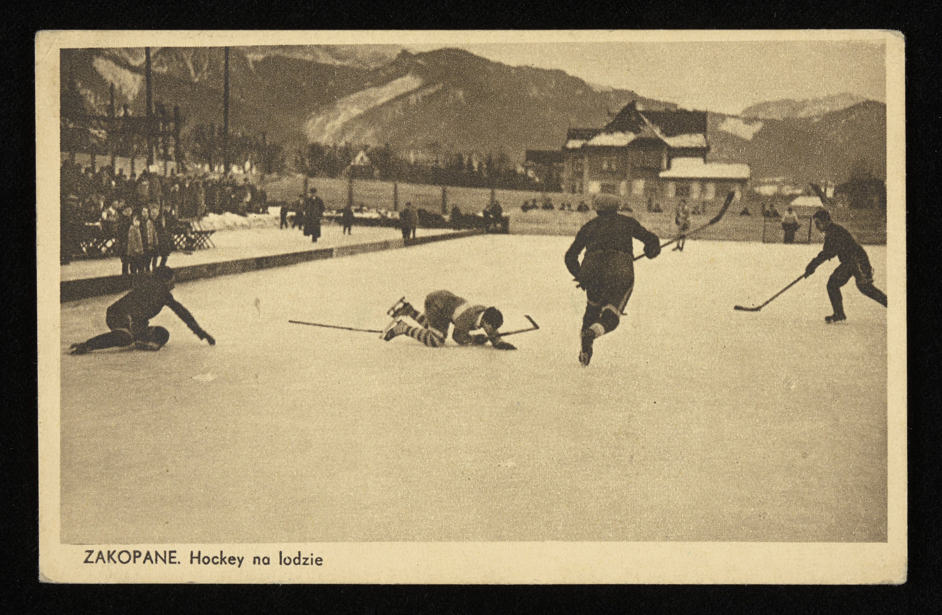 Schwarzes und weißes Foto von Menschen, die Hockey auf einem Eisstadion spielen, mit Gebäuden, Bäumen, Pfählen und Bergen im Hintergrund, einschließlich Text unten.
