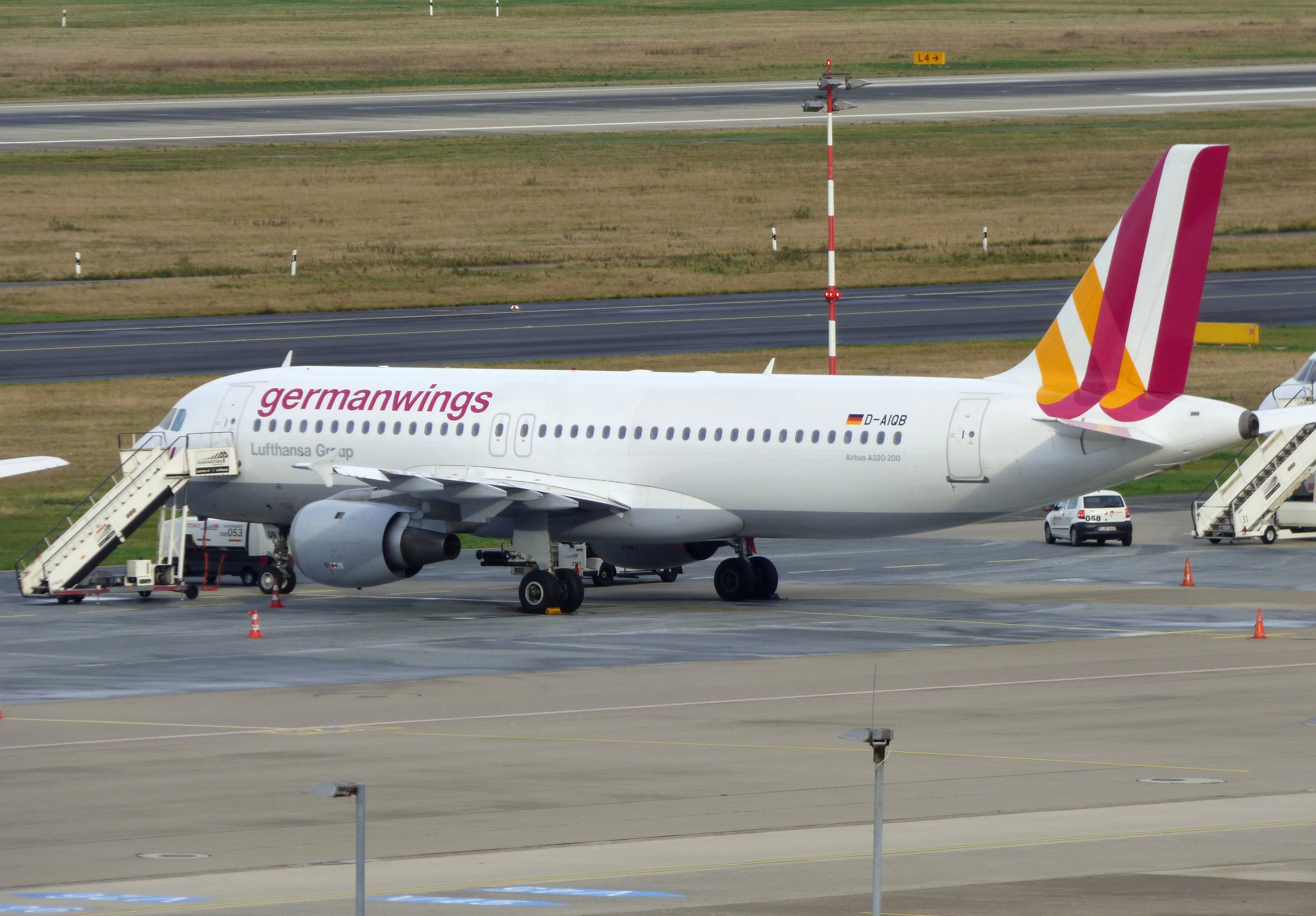 Germanwings Airbus A320-200 auf dem Frankfurter Flughafen geparkt mit Bodenfahrzeugen, Verkehrskegeln, Versorgungsmasten und Grasfläche im Hintergrund.
