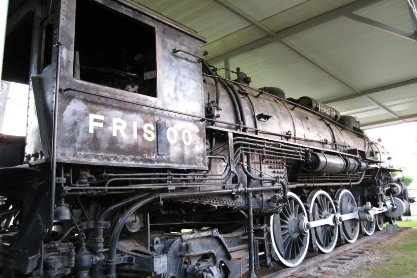 Ein Zug ist auf Eisenbahnschienen mit Gras darunter und einer Decke mit Pfählen darüber zentriert.