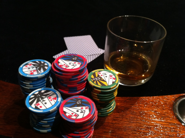 Eine hölzerne Oberfläche mit Münzen, ein schwarzes Tuch mit Karten und ein Glas mit Flüssigkeit.