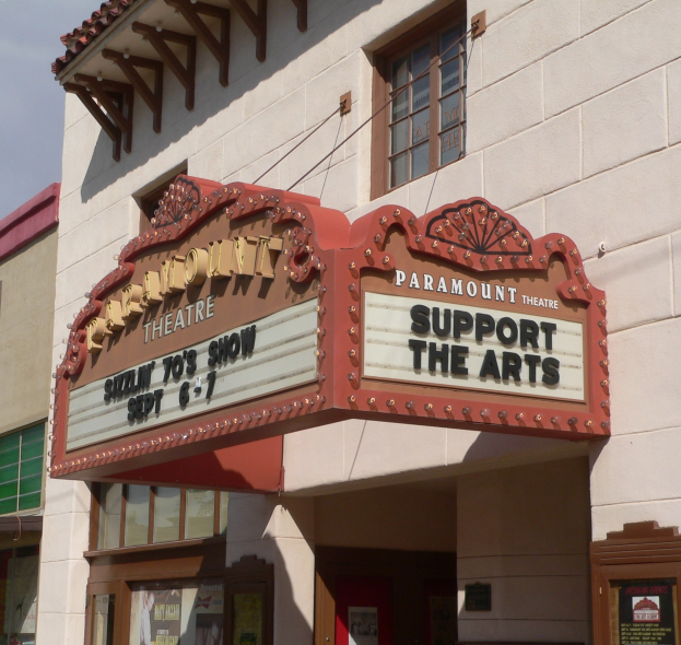 Das Paramount Theatre in Sacramento, Kalifornien, mit Glasfenstern und -türen, einer 'Unterstützt die Künste'-Schrifttafel und einem sichtbaren Himmel im Hintergrund.