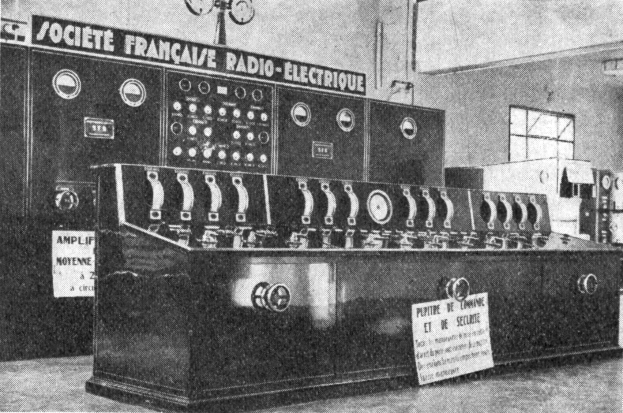 Ein Schwarz-Weiß-Foto eines altmodischen Radios auf einer Oberfläche, mit einer Wand, einem Fenster und anderen Gegenständen im Hintergrund und einem Text unten, der "Societe Française Radio Electrique" lautet.