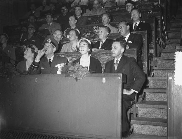 Ein Schwarz-Weiß-Foto einer Menge in einem Stadion mit einem Podium und einem Blumenstrauß davor und einer Treppe auf der rechten Seite.