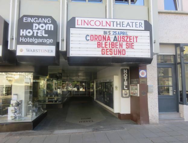 Das Lincoln Theater in Berlin, Deutschland, ein Gebäude mit Glasfenstern und -türen und einer Tafel mit Text darauf, mit verschiedenen Objekten im Inneren, die einen belebten Stadtbild einflößen.