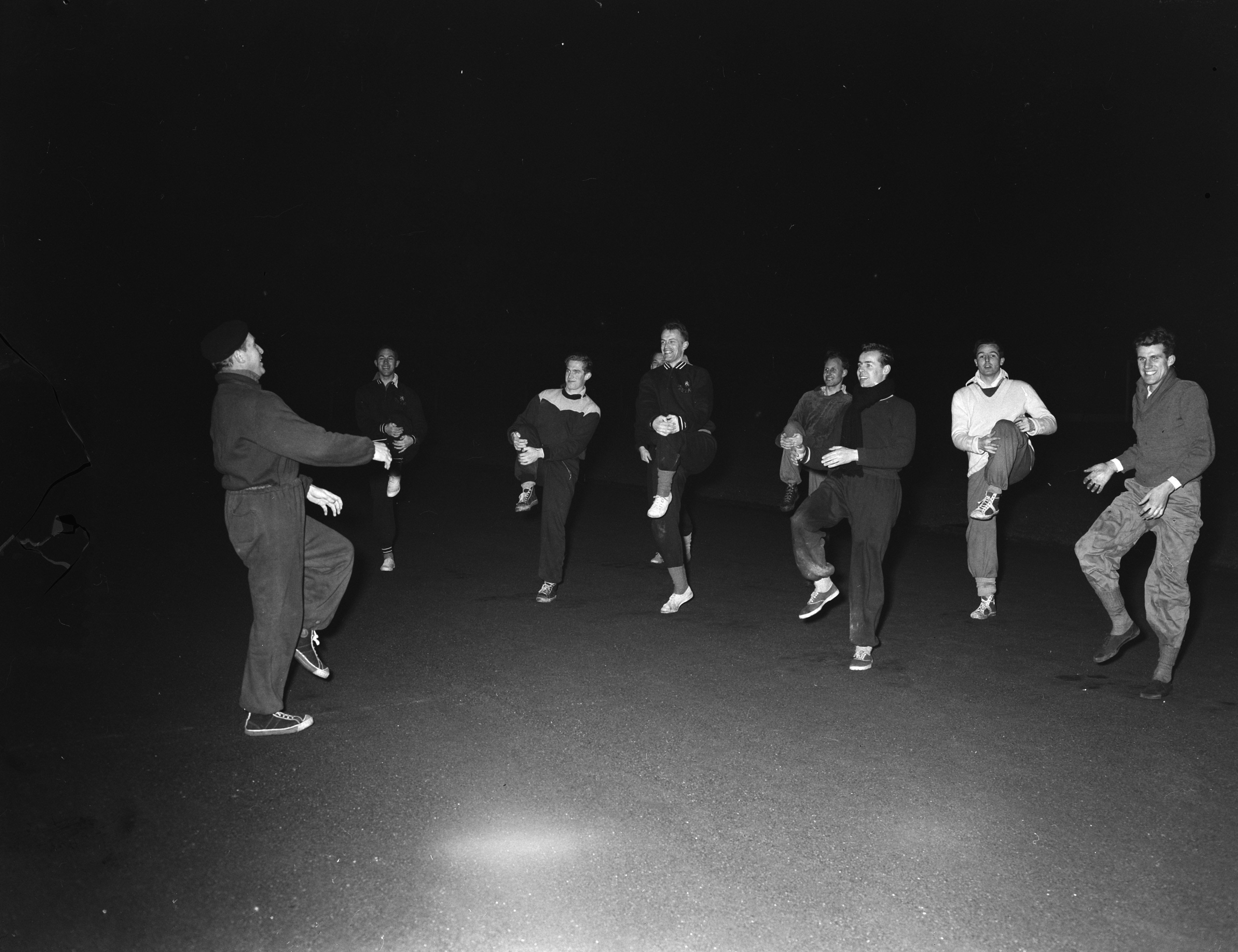 Eine Gruppe von Männern auf einer Bühne in einem Schwarz-Weiß-Setting, alle tragen Schuhe und scheinen mitten in einer Performance zu sein.