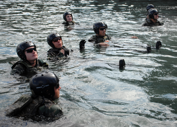 Eine Gruppe von Menschen in Helmen und Schwimmbrillen, die in ruhigem, klarem Wasser unter einer strahlenden Sonne schwimmen und in dieselbe Richtung bewegen.
