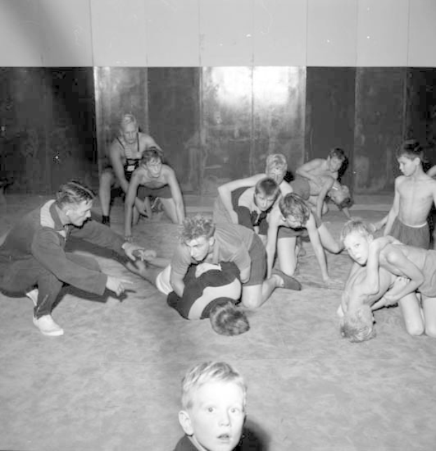 Schwarz-weißes Bild von jungen Jungs, die in einem Gym rängeln, mit einer Wand im Hintergrund.