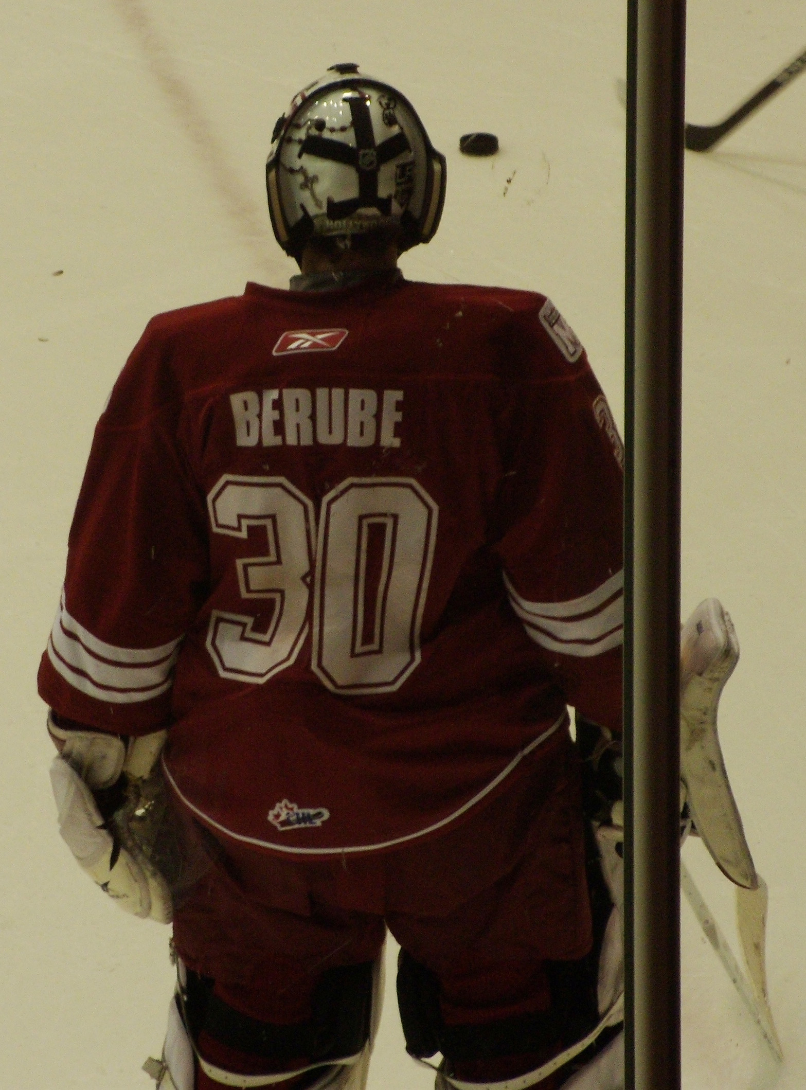 Ein Hockey-Spieler in Helm, Handschuhen und nummeriertem Trikot steht auf dem Eis vor einem Tor mit einem Pfahl rechts daneben.