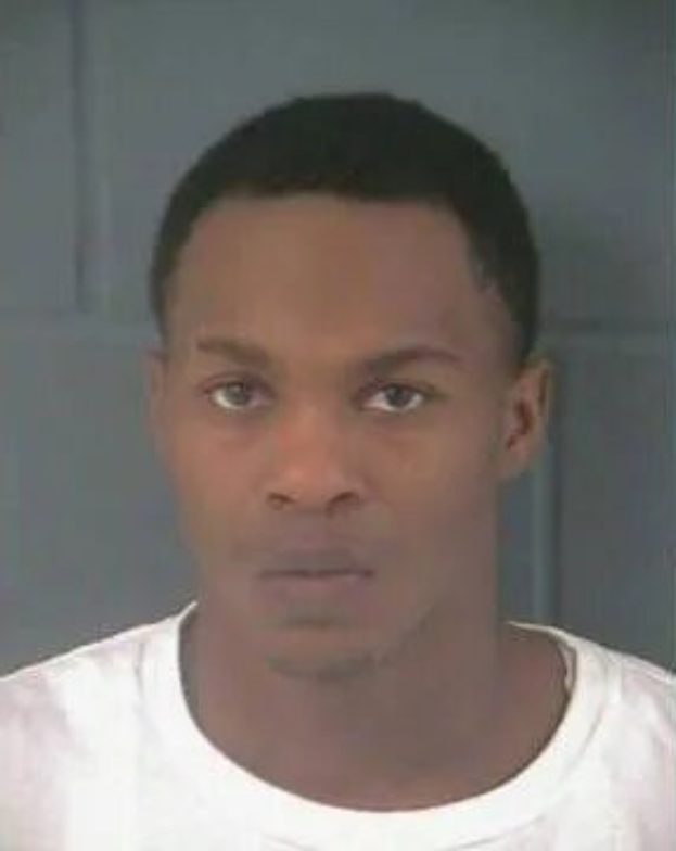 Ein Bild eines Mannes in einem weißen T-Shirt vor einer Wand, der mutmaßlich der Töter eines Mordfalls ist.