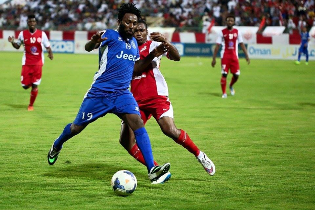 Eine Gruppe von Männern, die Fußball auf einem Feld spielen, tragen Benfica-Farben, mit Zuschauern und Werbetafeln im Hintergrund.