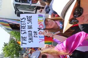 Eine Gruppe von Menschen steht vor einem Lkw und hält ein Schild mit der Aufschrift "Die Straßen sollten sicher sein". Einige tragen Mützen und Schutzbrillen, andere halten Schilder, und im Hintergrund sind Bäume, Gebäude und ein klarer blauer Himmel zu sehen.