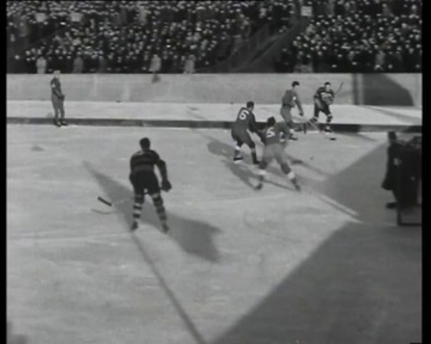 Schwarzes und weißes Foto von Männern, die Hockey auf einem Eisstadion spielen, mit Zuschauern auf den Tribünen im Hintergrund.