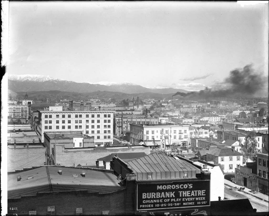 Ein Schwarz-Weiß-Bild eines Fabrikgebäudes mit Rauch, der aus seinem Schornstein aufsteigt und von Gebäuden umgeben ist.