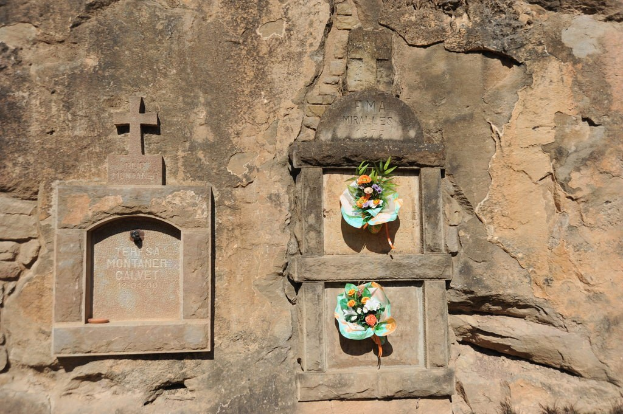 Gedenktafeln in eine Wand gemeißelt mit Blumensträußen davor.