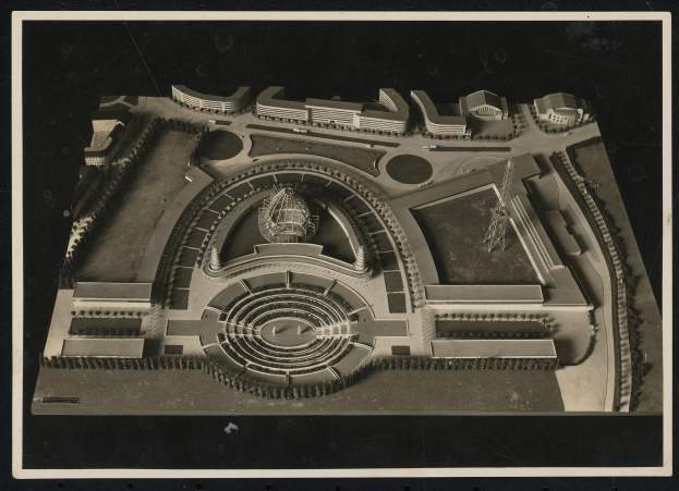 Schwarzes und weißes gerahmtes Foto eines detaillierten Modellkonzertsaals mit einer zentralen Kuppel, Steinwänden, Metalldach und einer hell beleuchteten Bühne, umgeben von einer Menge.