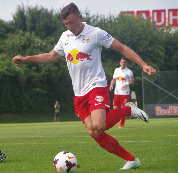 Ein professioneller Fussballspieler, der einen Ball auf einem grünen Feld kickt, mit «RB Leipzig» im Hintergrund.