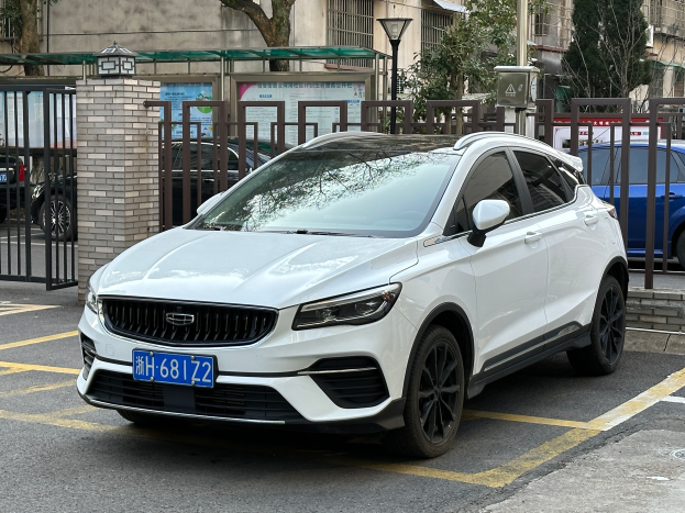 Ein weißer Volvo XC40 T5 AWD Inscription auf einem Parkplatz mit Gebäuden, Bäumen, Polen, Lampen und anderen Objekten im Hintergrund.