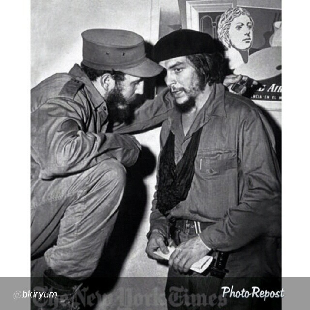 Zwei Personen unterhalten sich vor einem gerahmten Bild und einer Wand, mit Text am unteren Bildrand.