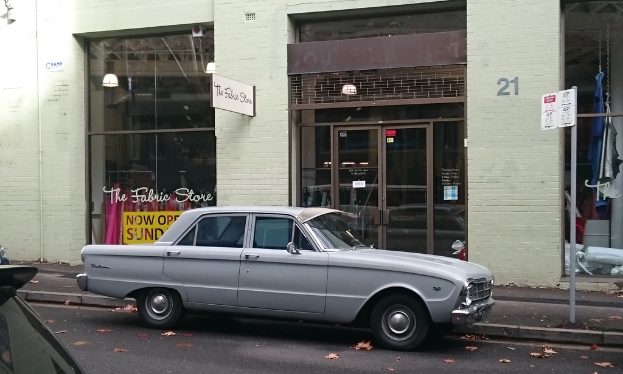 Ein silbernes Auto parkt auf einer Straße vor einem Gebäude mit mehreren Türen, und in der Nähe ist ein Schild mit Text zu sehen.