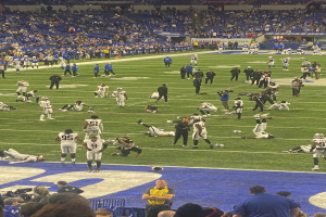 Ein Fußballspiel wird in einem Stadion mit Zuschauern auf dem Rasen und einigen auf Stühlen im Hintergrund sowie einer Person mit einer Kamera gespielt.