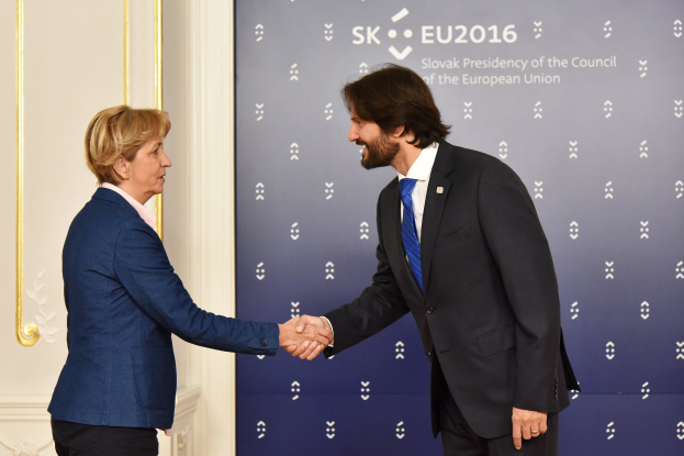 Bundeskanzlerin Angela Merkel und Bundeskanzler Joachim Gauck schütteln sich die Hände vor einer Wand mit einem Banner "EU-Gipfel" und einer Tür im Hintergrund, beide lächeln.