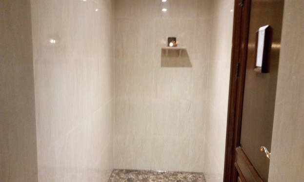 Badezimmer mit einer Duschwanne, Toilette und Tür auf der rechten Seite, mit Fliesenwänden und Deckenleuchten.