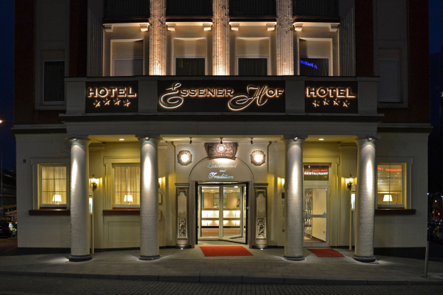 Das Essenerhof Hotel in Berlin, Deutschland, ein mehrstöckiges Gebäude mit Fenstern, Türen, Säulen, Lampen und einem Namensschild, mit einer Straße rechts daneben, unter einem klaren Himmel.