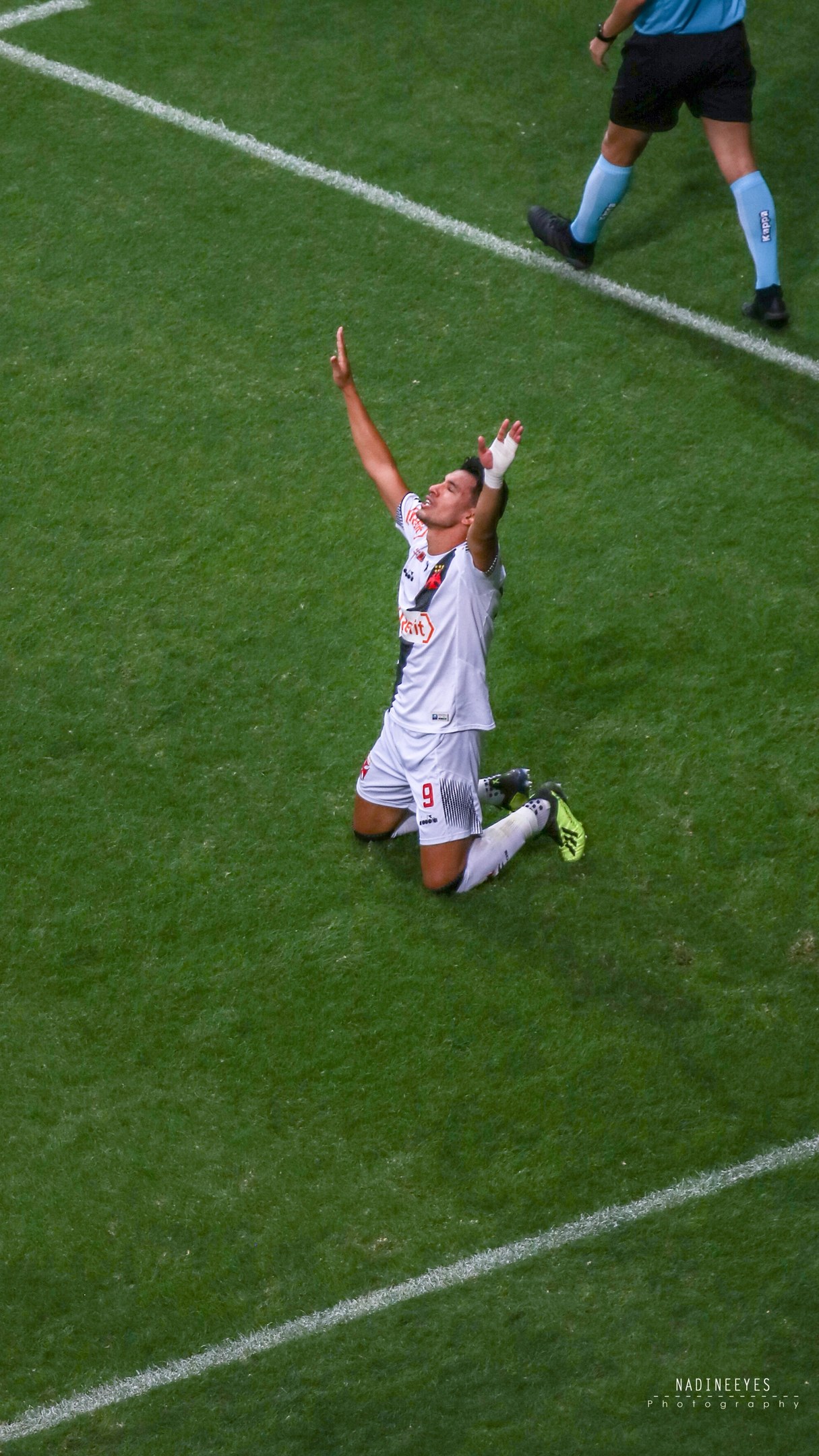 Ein Fußballspieler in Uniform kniet auf dem Boden und feiert mit ausgestreckten Armen.